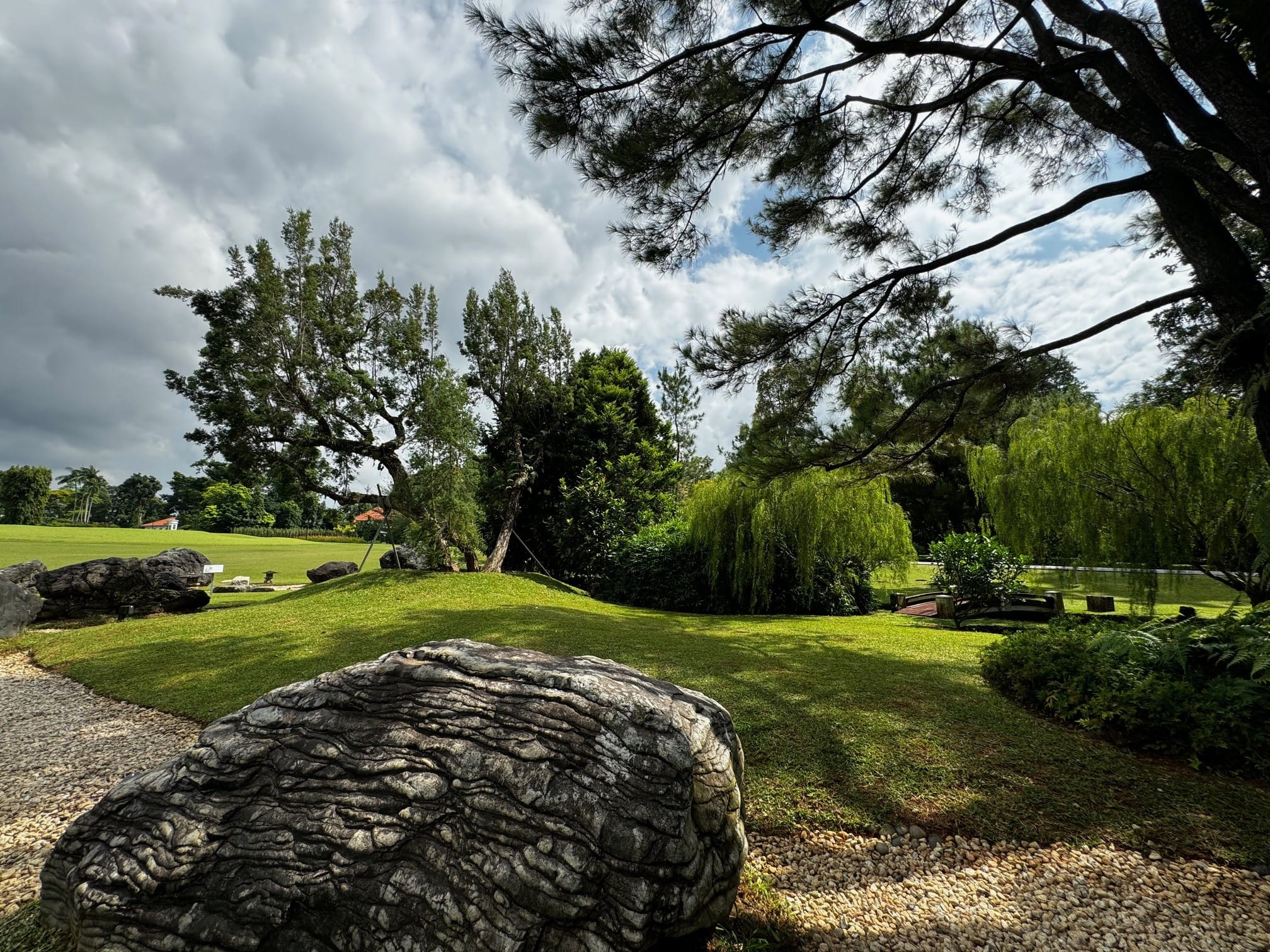 Landscape with textured rock, grass lawn, trees, and cloudy sky overhead.